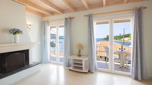 Una habitación amplia con chimenea, una mesita con una lámpara y vistas al mar a través de grandes ventanales.