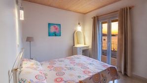 Un dormitorio con cama, mesita de noche, lámpara, un cuadro y vistas al exterior.
