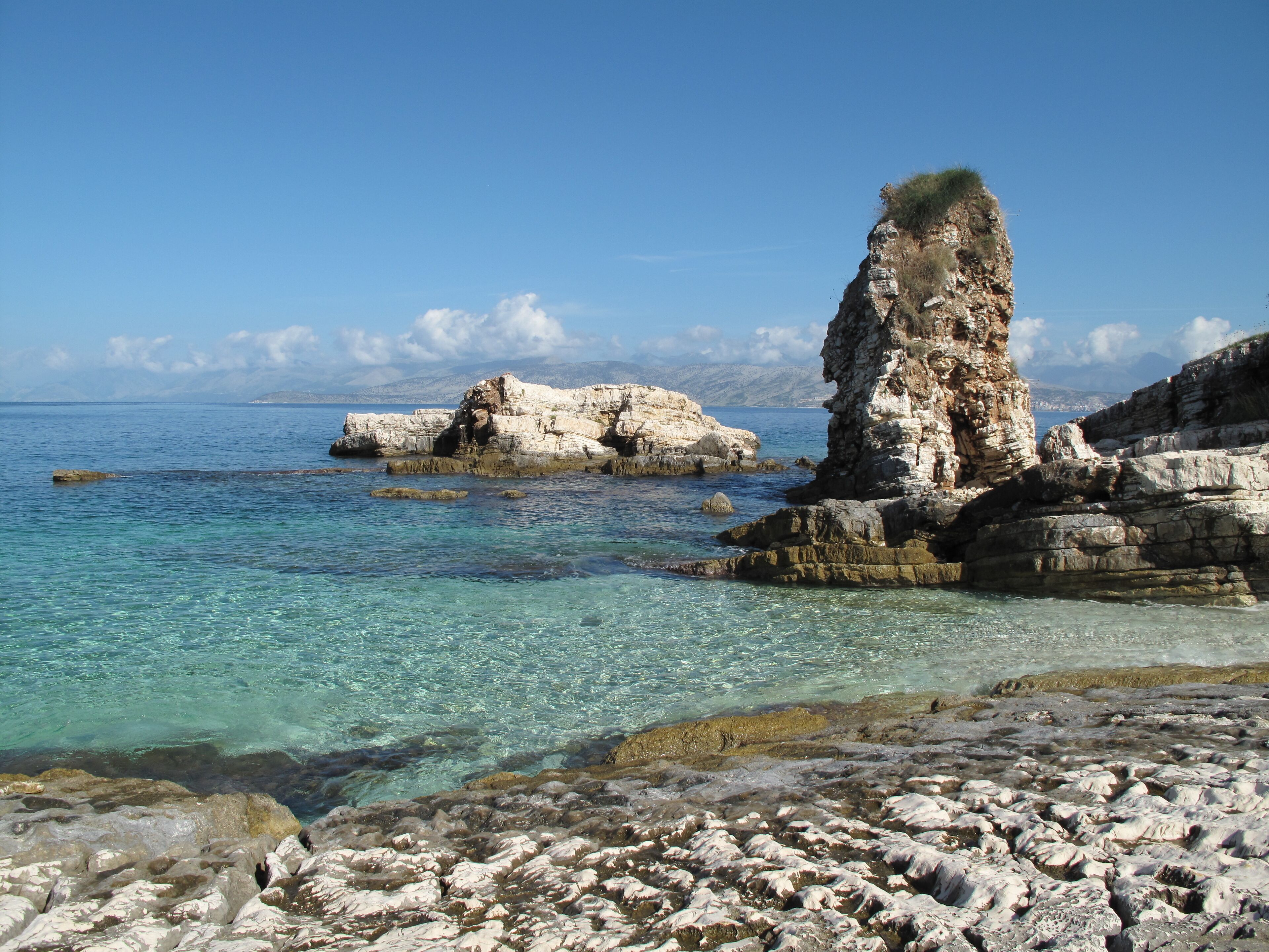 Une côte rocheuse bordée d’eaux d’un bleu limpide et surmontée d’une formation rocheuse blanche imposante.