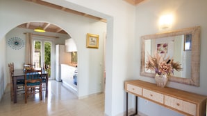 Un comedor con mesa y sillas de madera, una consola con espejo y florero, y un arco que da a la cocina.