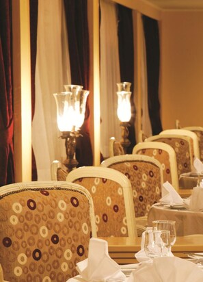A dining area with patterned chairs, tables set with white tablecloths, and two lit lamps. -  Mövenpick Prince Abbas Lake Nasser Cruise, Every Monday Four Nights From Aswan, Every Friday Three nights From Abu-Simbel - Including Excursions and Sightseeing (Aswan)