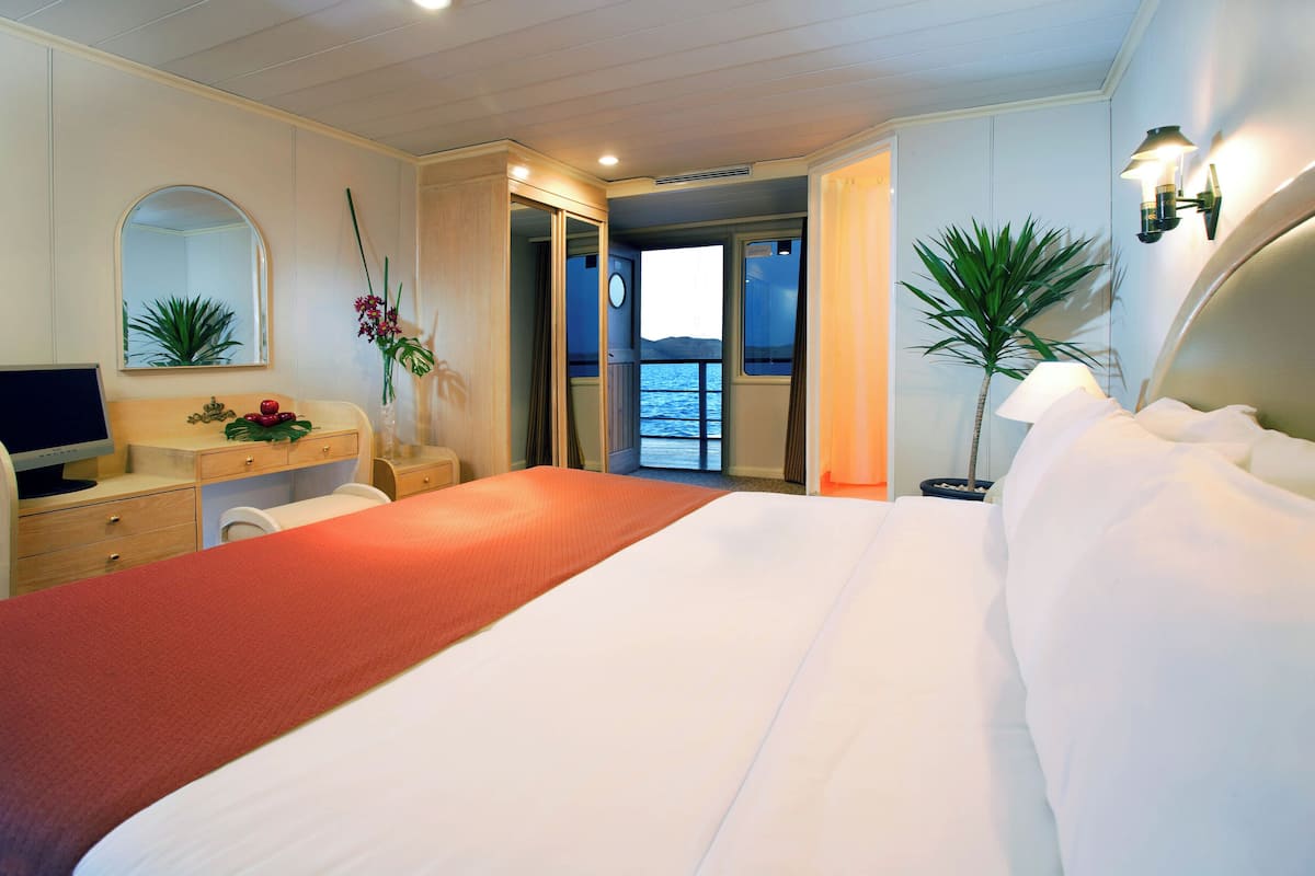 A hotel room with a large bed, a desk with a computer, a mirror, and a view of the sea.