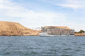 A large cruise ship docked at a port with a sandy cliff in the background. -  Mövenpick Prince Abbas Lake Nasser Cruise, Every Monday Four Nights From Aswan, Every Friday Three nights From Abu-Simbel - Including Excursions and Sightseeing (Aswan)