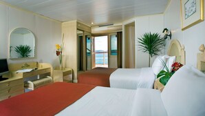 Quarto de hotel com duas camas, uma escrivaninha com cadeira, um espelho e vista para o mar.