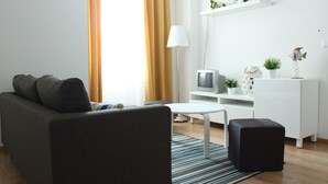 A modern living room with a grey sofa, a white coffee table, a black ottoman, and a TV on a white stand. - Aveiro White House (Aveiro)