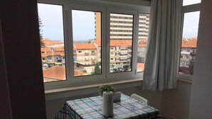 A room with a table covered by a plaid tablecloth, a potted plant, and a view of buildings through large windows. - Aveiro White House (Aveiro)