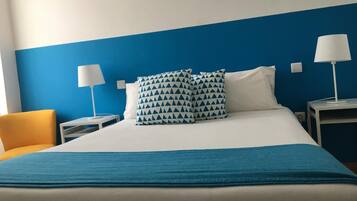 A hotel room with a bed, two bedside tables, two lamps, a blue wall, and a yellow chair.
