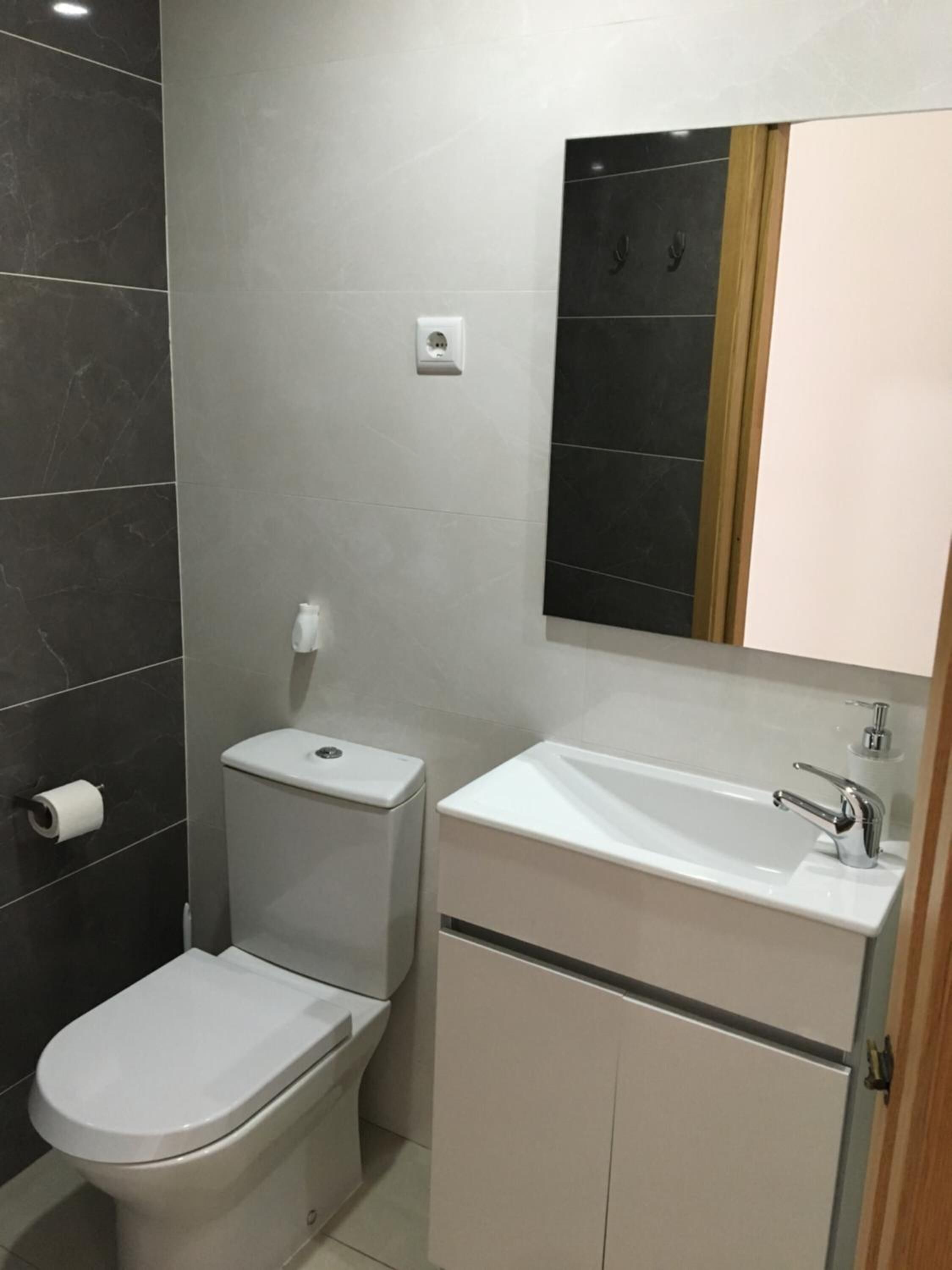 Un baño moderno con inodoro, lavamanos y espejo.