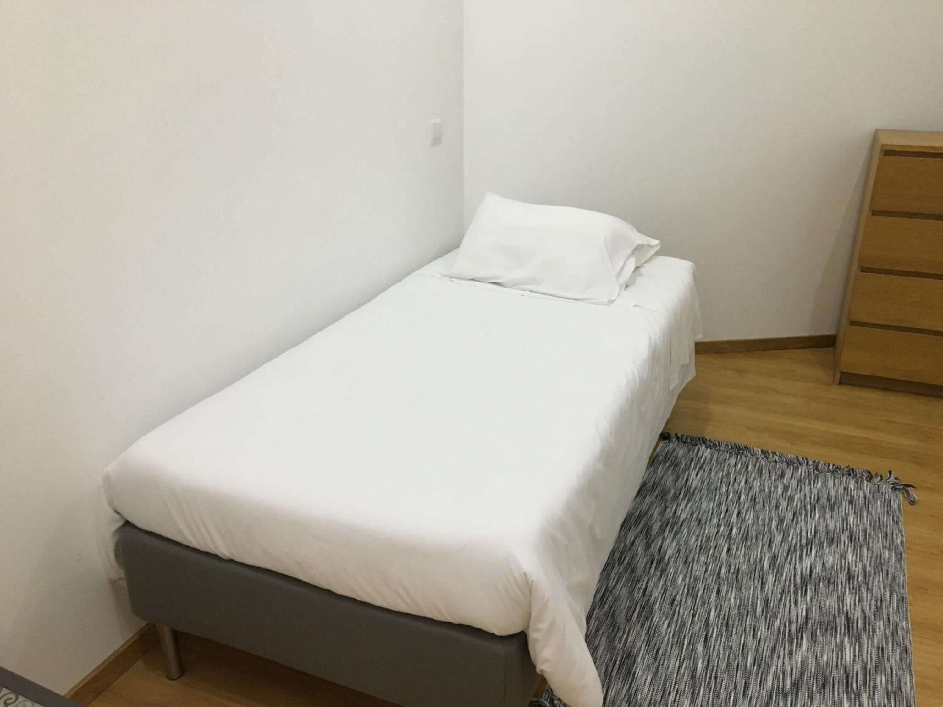 Una cama pequeña y ordenada con ropa blanca en una habitación compacta.