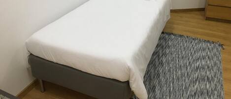Una cama pequeña y ordenada con ropa blanca en una habitación compacta.