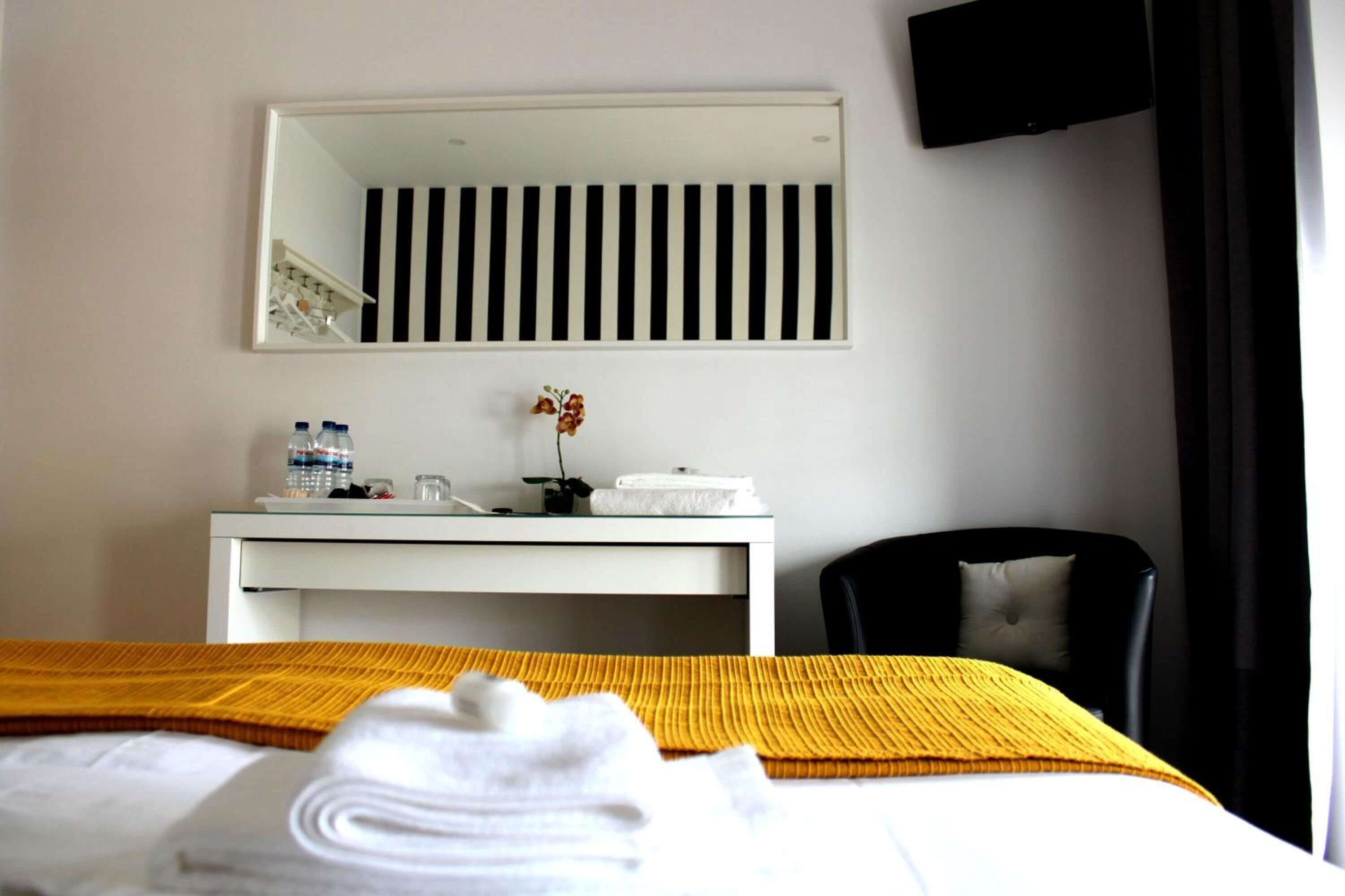 Una habitación de hotel con cama, escritorio con espejo, silla y televisión en la pared.