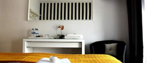 Una habitación de hotel con cama, escritorio con espejo, silla y televisión en la pared.