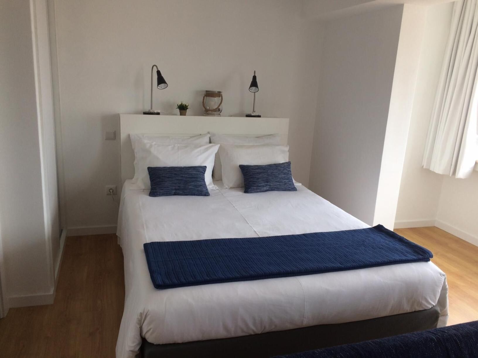 A neatly made bed with white bedding and two dark blue pillows, a bedside lamp, and a small decorative item on the nightstand.