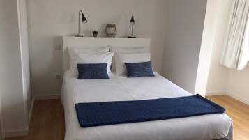 A neatly made bed with white bedding and two dark blue pillows, a bedside lamp, and a small decorative item on the nightstand.