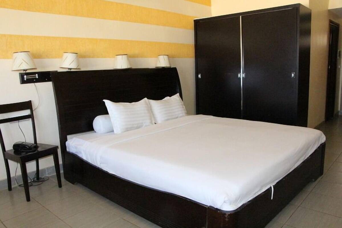 A neatly made bed with white linens, a dark headboard, and a black wardrobe with two doors.