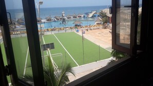 Une vue sur une piscine située au bord de la plage, avec une statue, une zone sablonneuse et un ciel bleu dégagé.