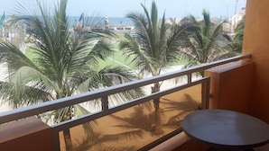 Un balcon avec vue sur des palmiers et une zone sablonneuse, une table ronde et une chaise.