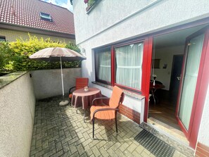 En terrasse med et bord og stole, en markise og et vindue med røde rammer.