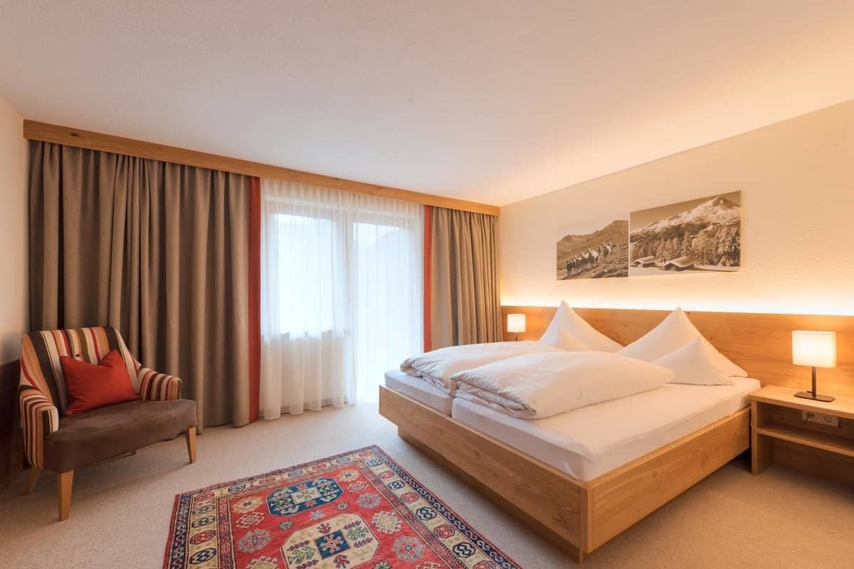 A hotel room with a large bed, a chair, a nightstand, and a rug.