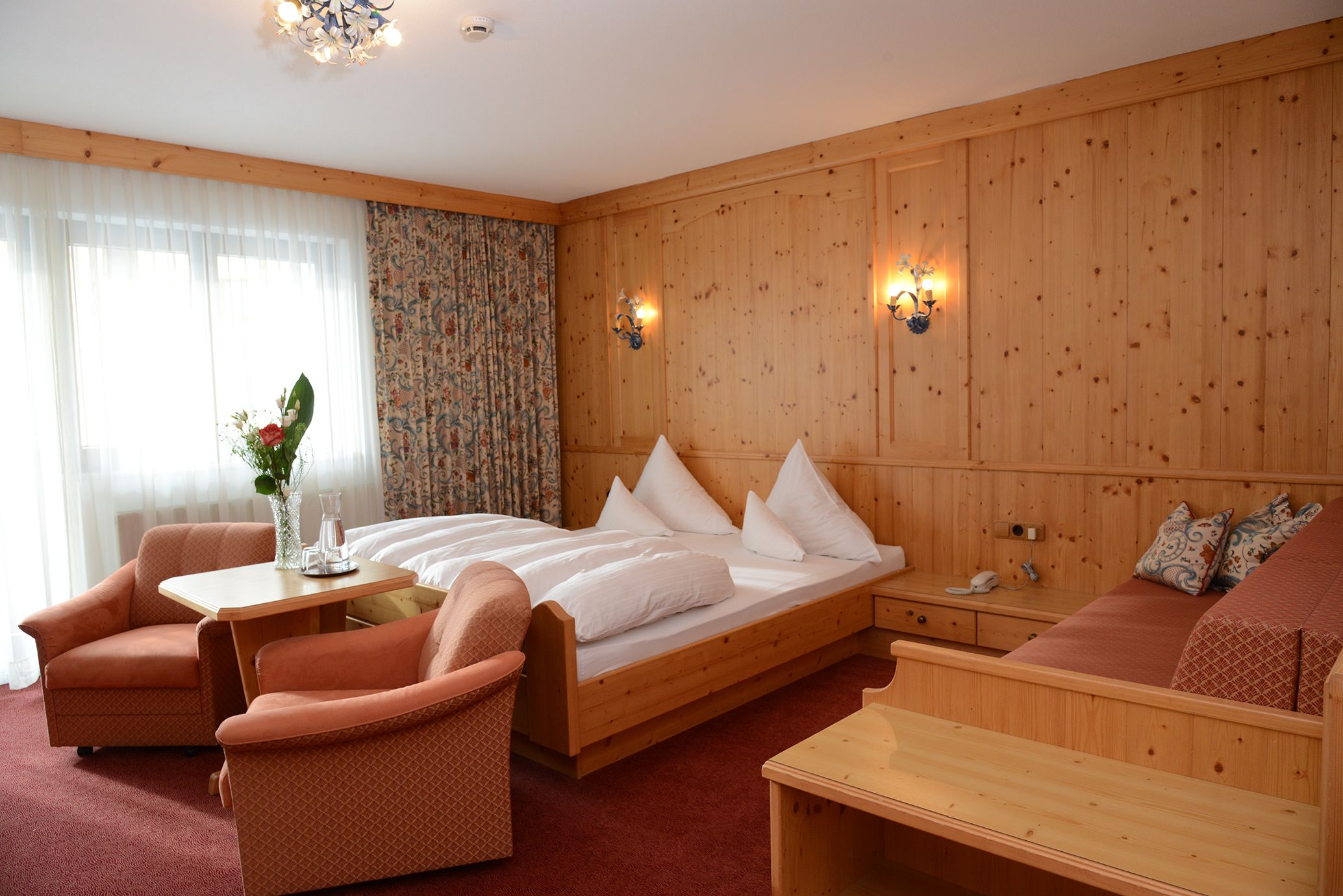 A wooden-paneled room with a bed, two armchairs, a small table, and a sofa.