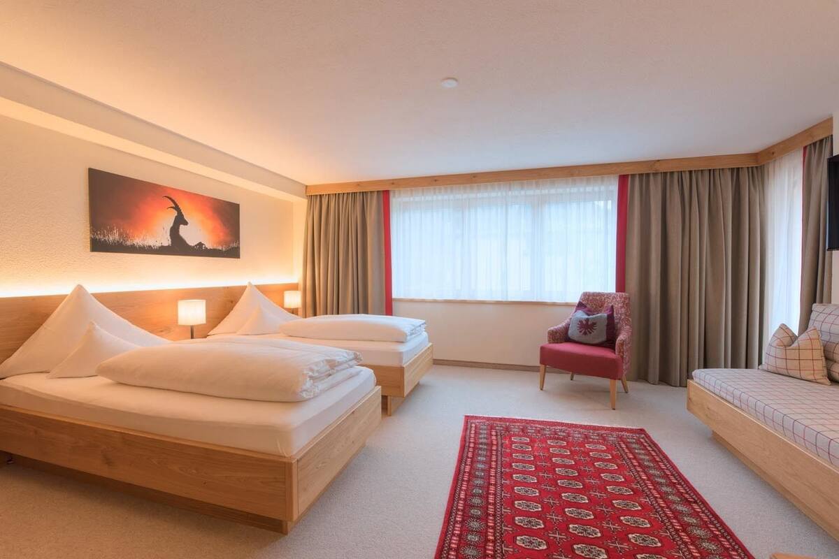 A hotel room with two beds, a red armchair, a red patterned rug, and a painting on the wall.