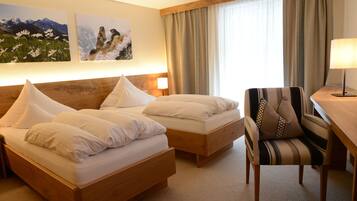 Een hotelkamer met twee houten bedden, een gestreept fauteuil, een bureau met een lamp en twee ingelijste foto's aan de muur.
