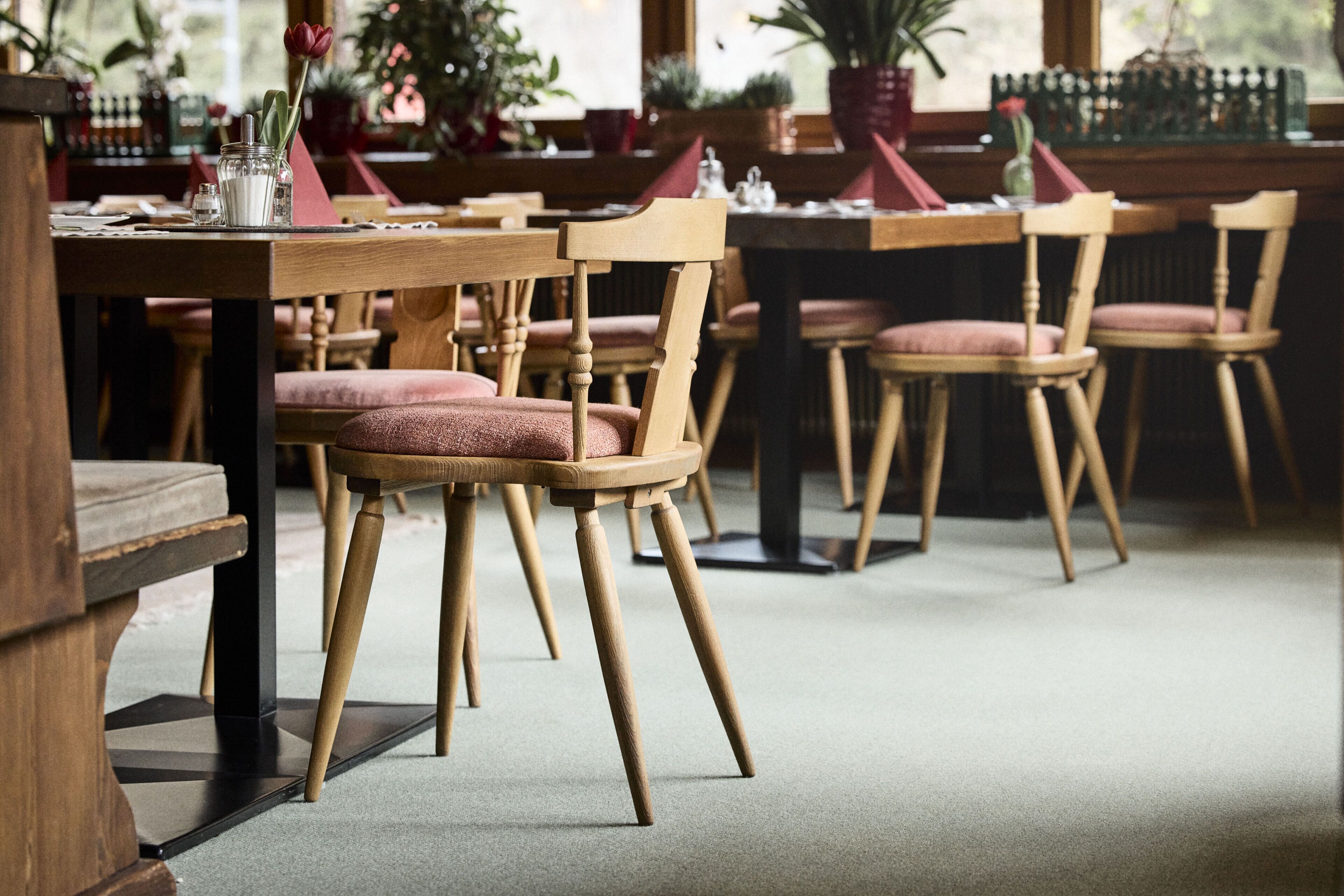 A restaurant interior with wooden tables and chairs, potted plants, and a cozy ambiance.