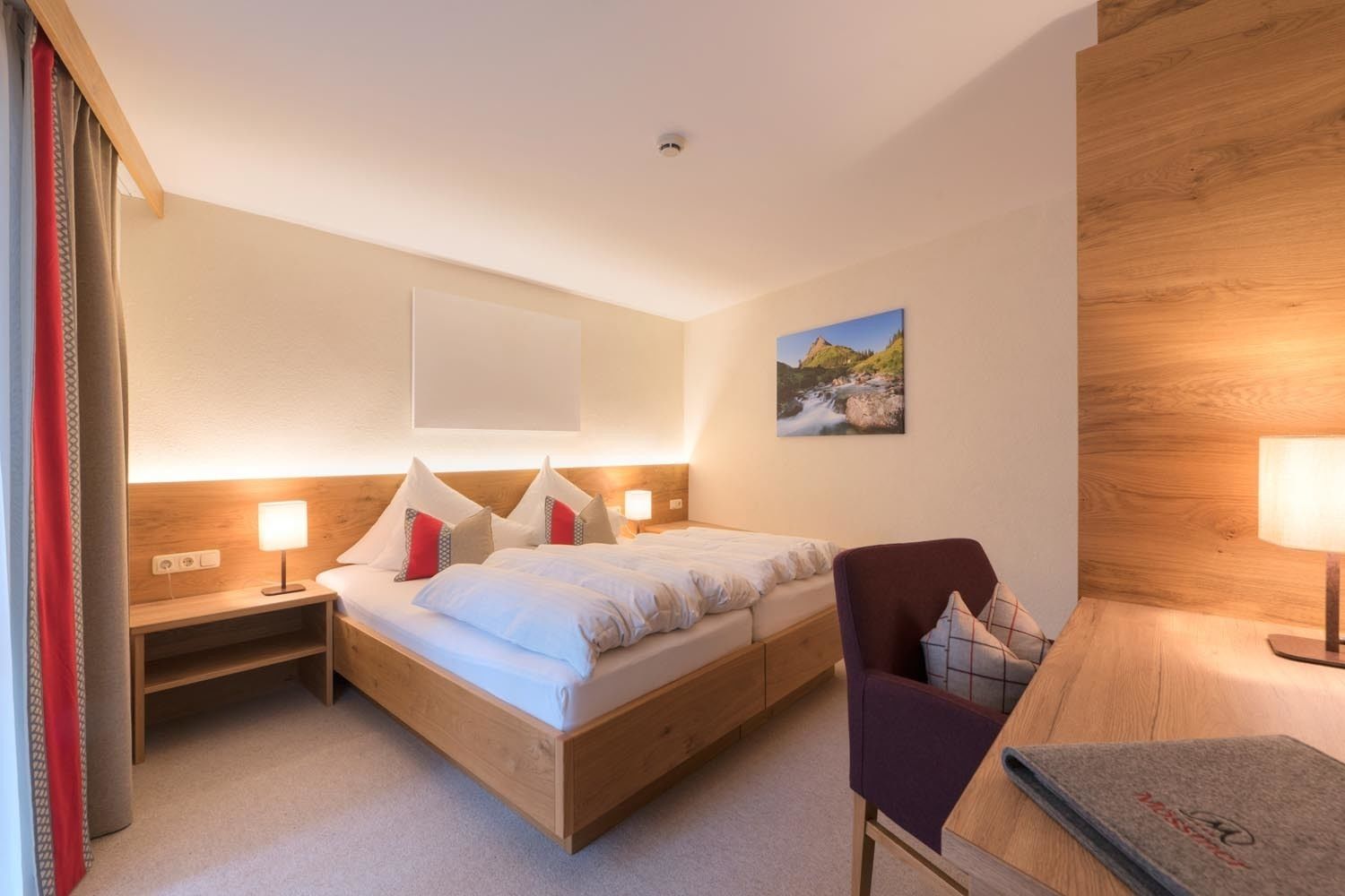 A hotel room with a wooden bed, two bedside tables with lamps, a chair, and a wall-mounted picture.