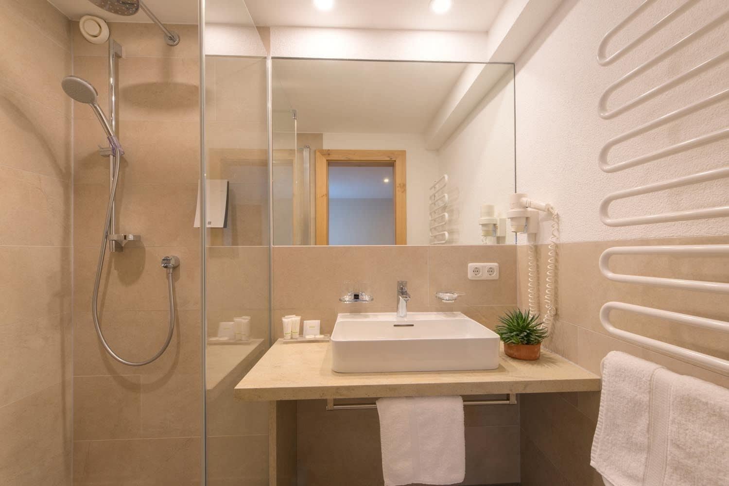 A modern bathroom with a glass shower enclosure, a white sink, and a towel rack.