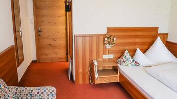 A hotel room with a wooden bed, a small bedside table with a phone, a floral pillow, and a patterned armchair.