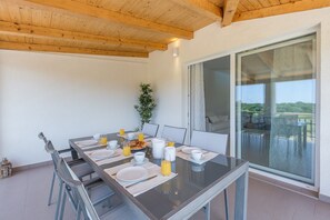 Comedor con mesa de vidrio, platos blancos, vasos y jugo de naranja, frente a una pared blanca y techo de madera.