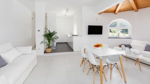 A modern, white-themed living space with a dining area, a sofa, a TV, and a window with a view of greenery. - Modern Villa Aria with beautiful garden and private Pool near Vrsar (Vrsar)
