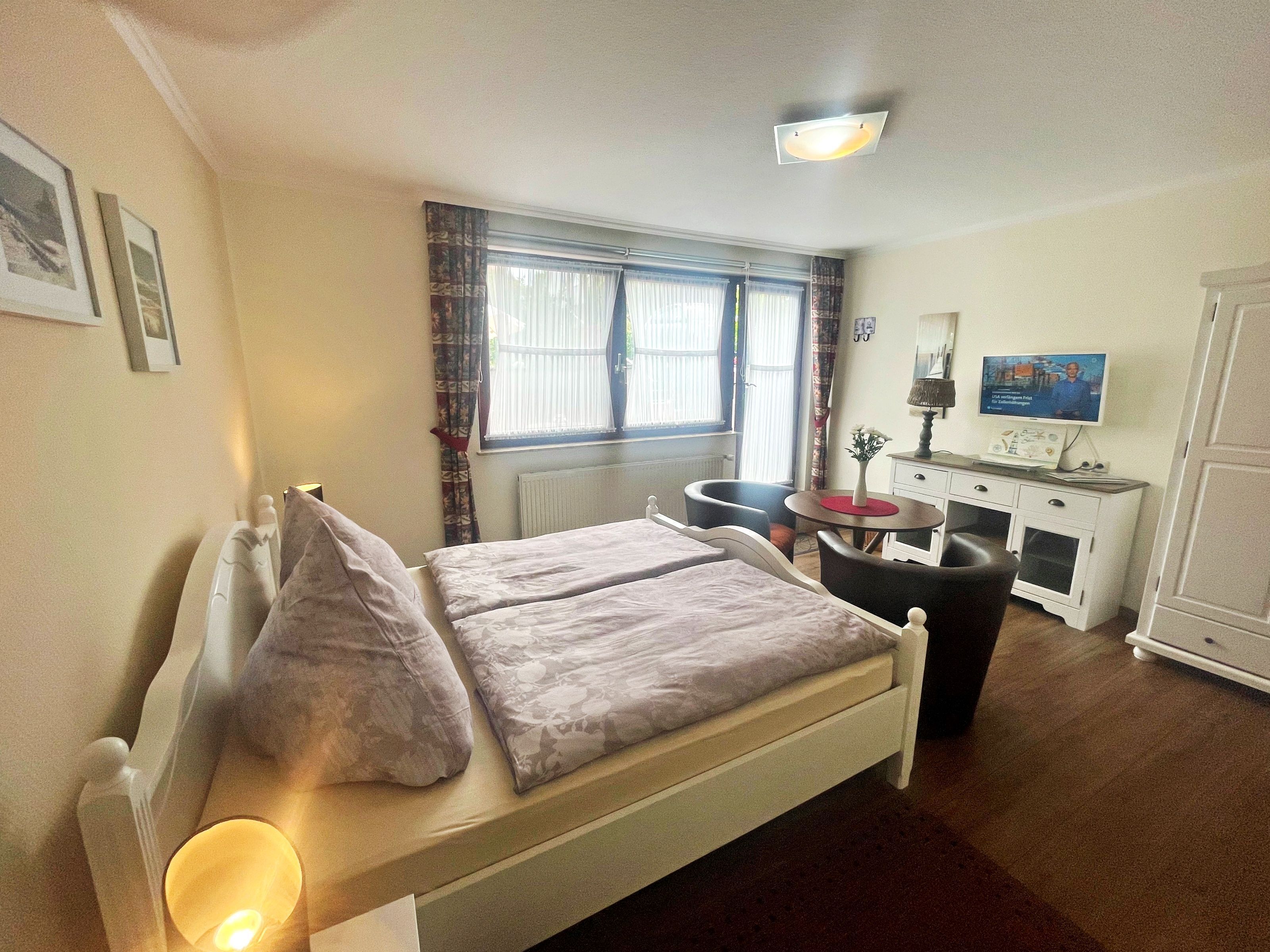 A bedroom with a bed, bedside table, lamp, and a TV on a dresser.