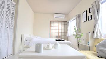 A hotel room with a bed, a bedside table with tea sets, a small plant, and a window with curtains.