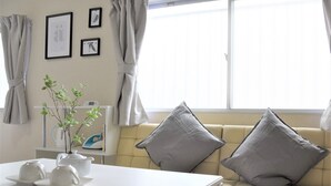 A living room with a sofa, cushions, a table with a teapot and cups, a plant, and framed pictures on the wall. - U-shuku Ar5 (Osaka)