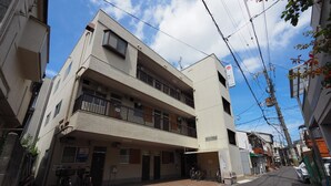 A multi-story building with a ground-level entrance, a covered parking area, and a visible signboard. - U-shuku Ar5 (Osaka)