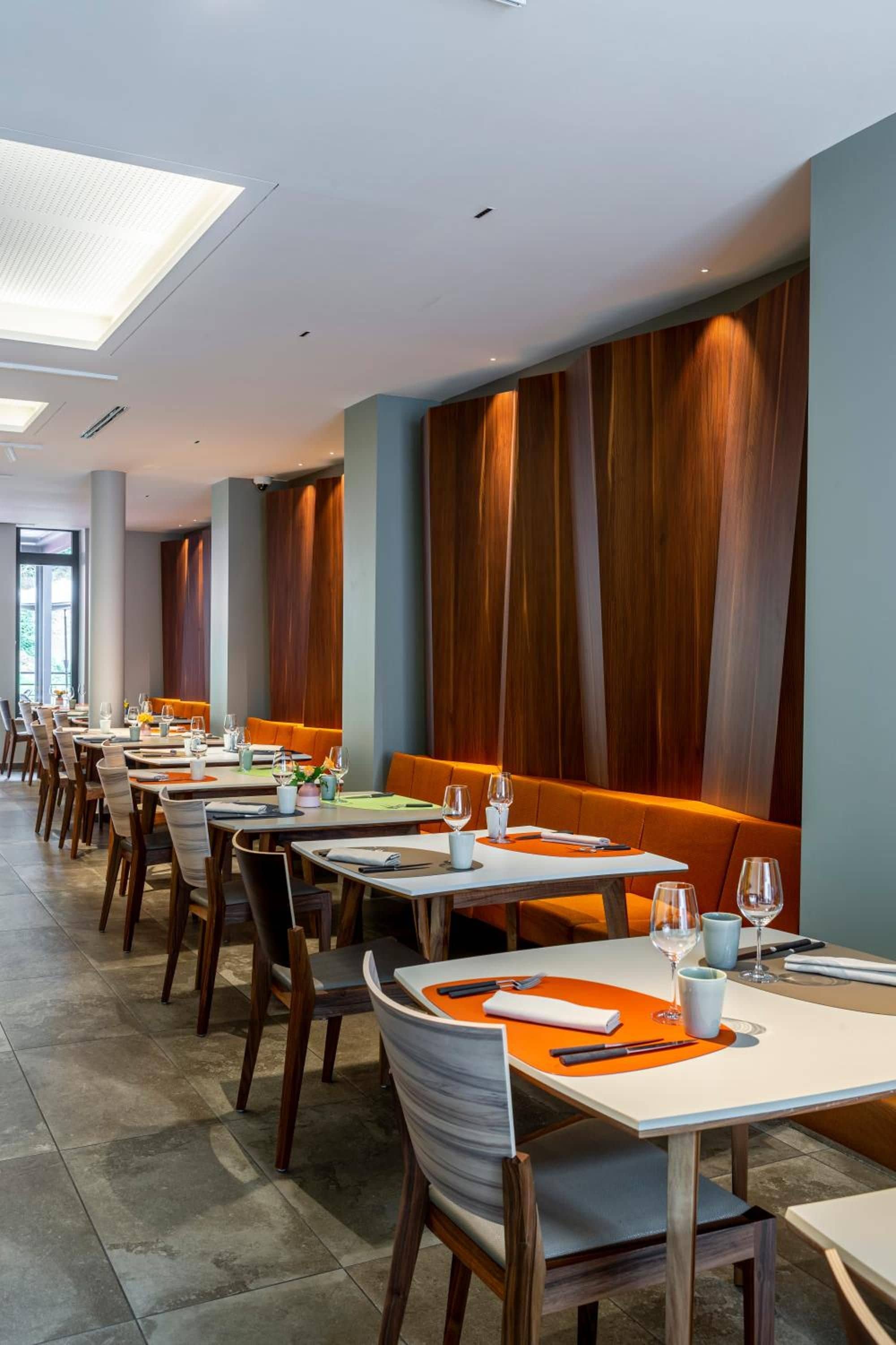 Ein Restaurant mit langen Tischen, Holzwandverkleidung und orangenen Sitzplätzen.