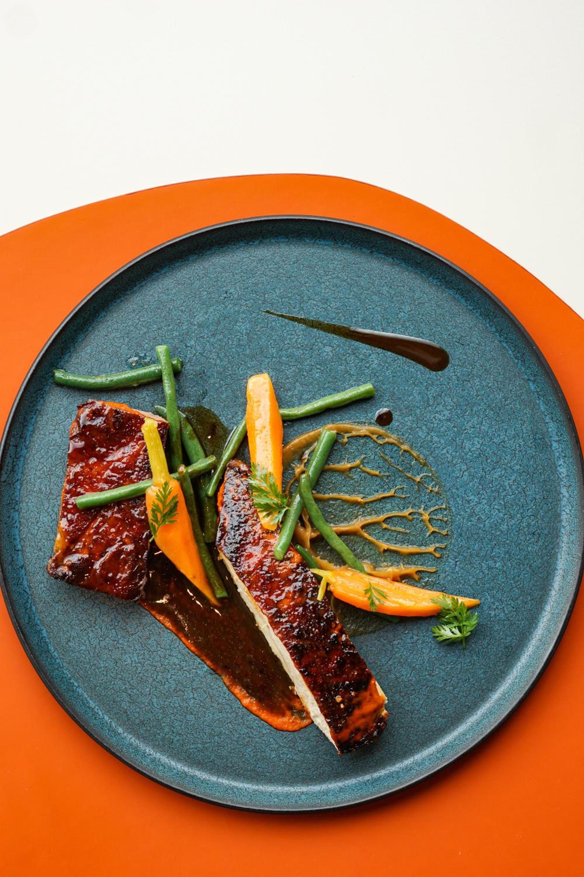 Un piatto con carne, fagiolini, carote e salsa.