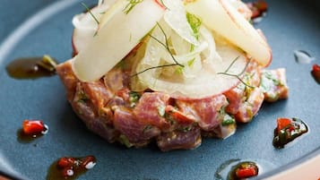 A dish with a base of minced meat, topped with thinly sliced onions and herbs, served on a dark plate with a blue rim.