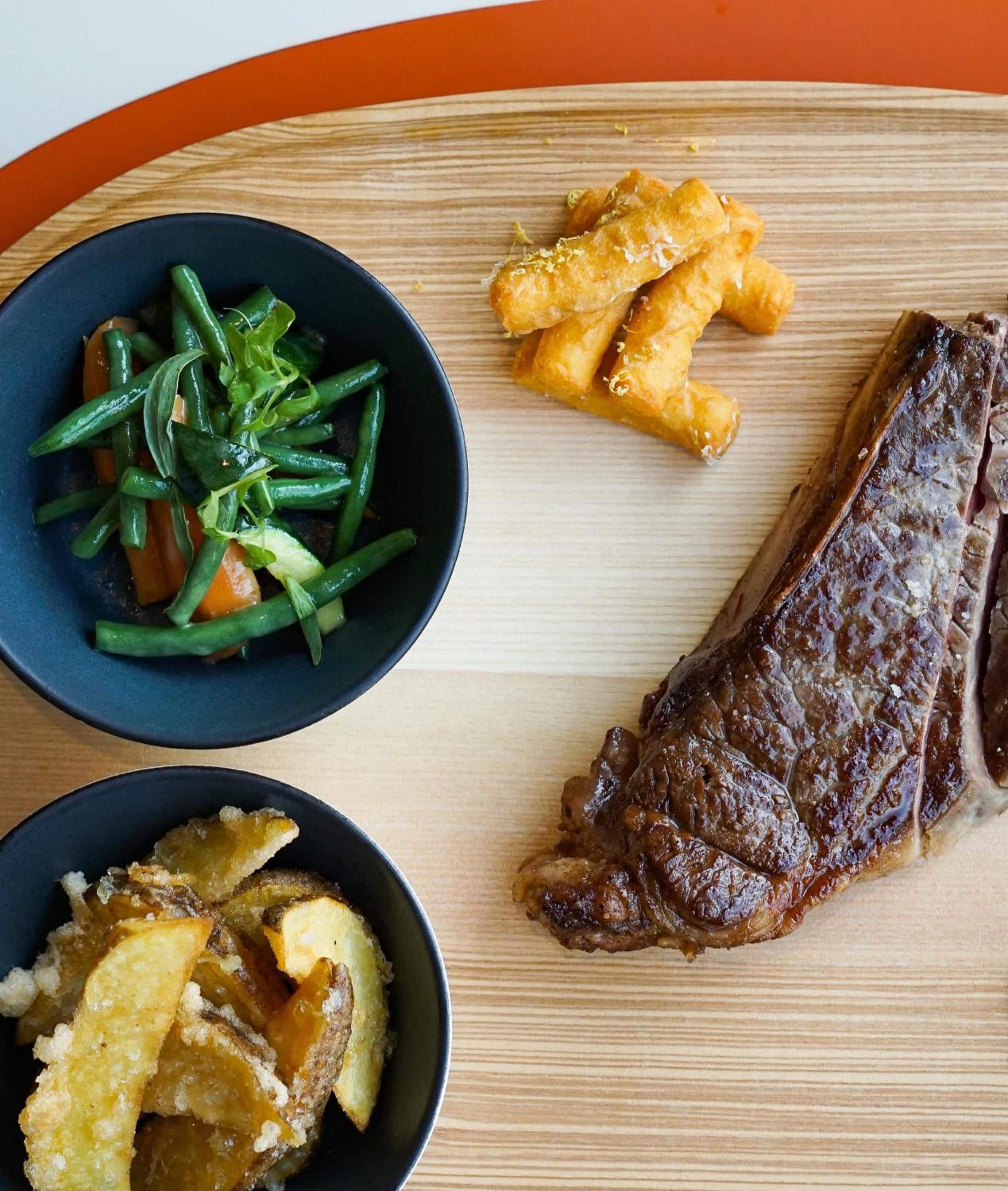 A wooden table with a steak, green beans, and fried items.