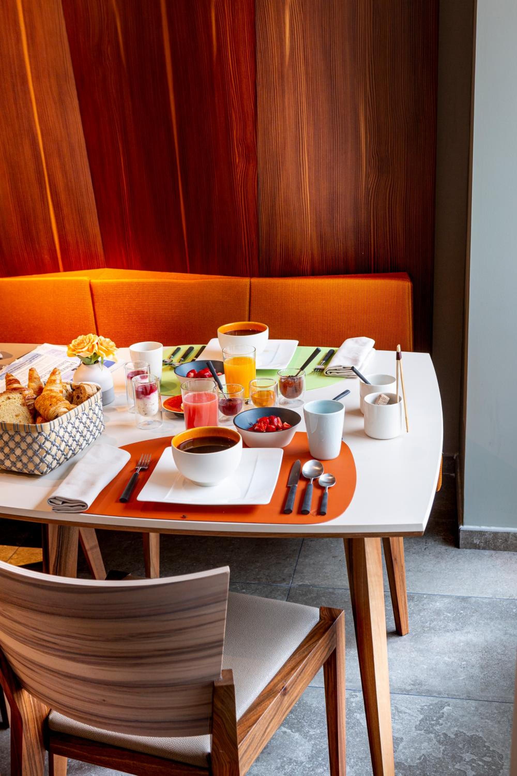 A dining table set with various breakfast items, a vase with a single flower, and a wooden chair.
