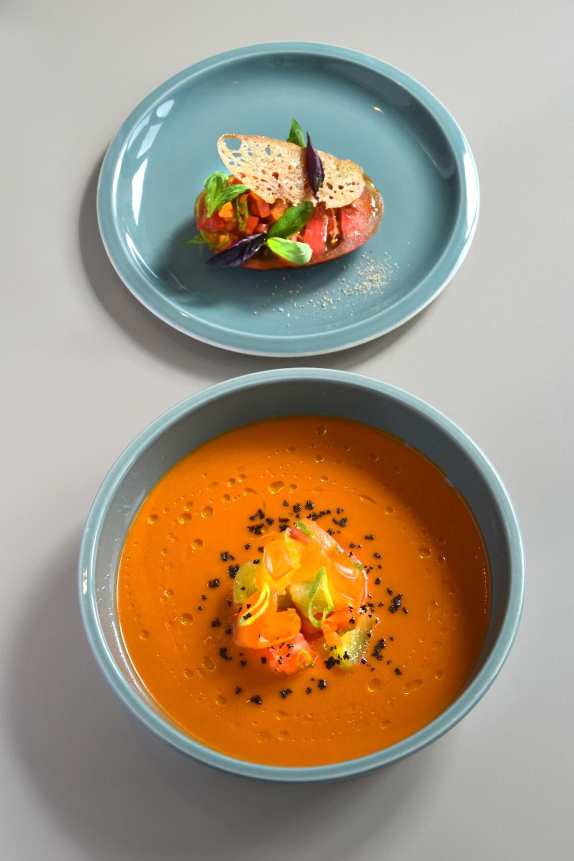 Two dishes, one with a soup and the other with a salad, on separate plates.