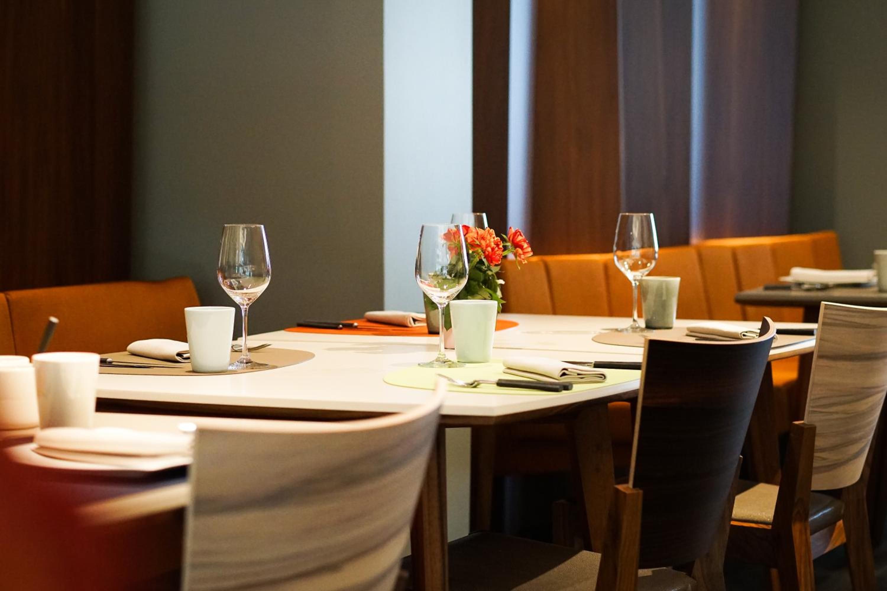 Ambiente de restaurante com mesas preparadas para refeições, incluindo cadeiras, pratos, talheres e copos.