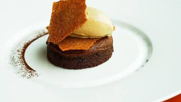 Un postre con base de brownie, cubierto con una bola de helado y un trozo de pan caramelizado.