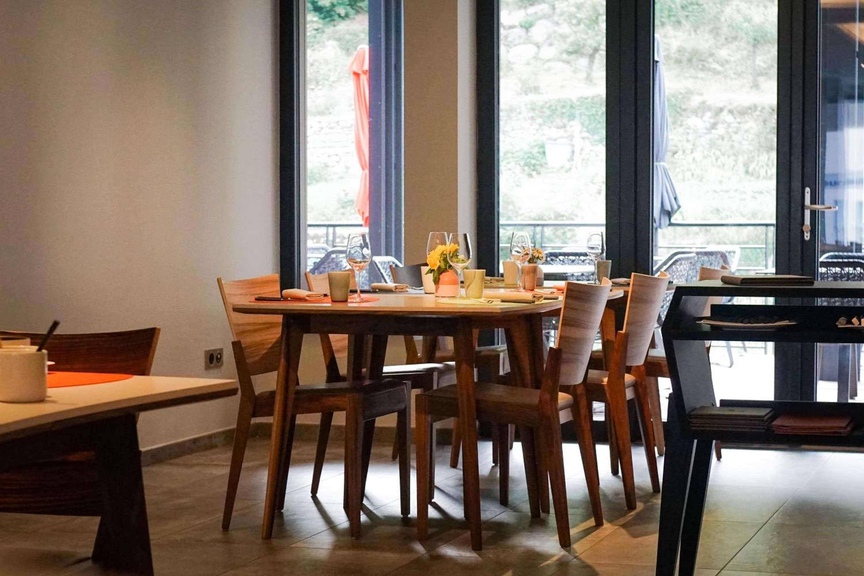 A dining area with a round table, chairs, and a view of the outdoors through large windows.