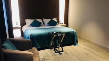 Quarto de hotel com uma cama, uma cadeira e uma mesinha.