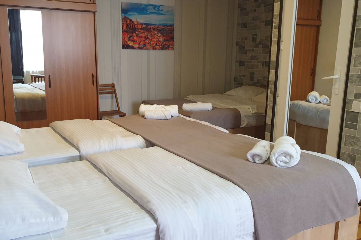 A hotel room with three beds, a painting on the wall, and a bathroom with a tiled shower area.