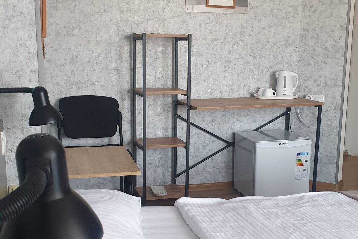 A hotel room with two beds, a desk with a chair, a small fridge, a lamp, and a picture frame on the wall.
