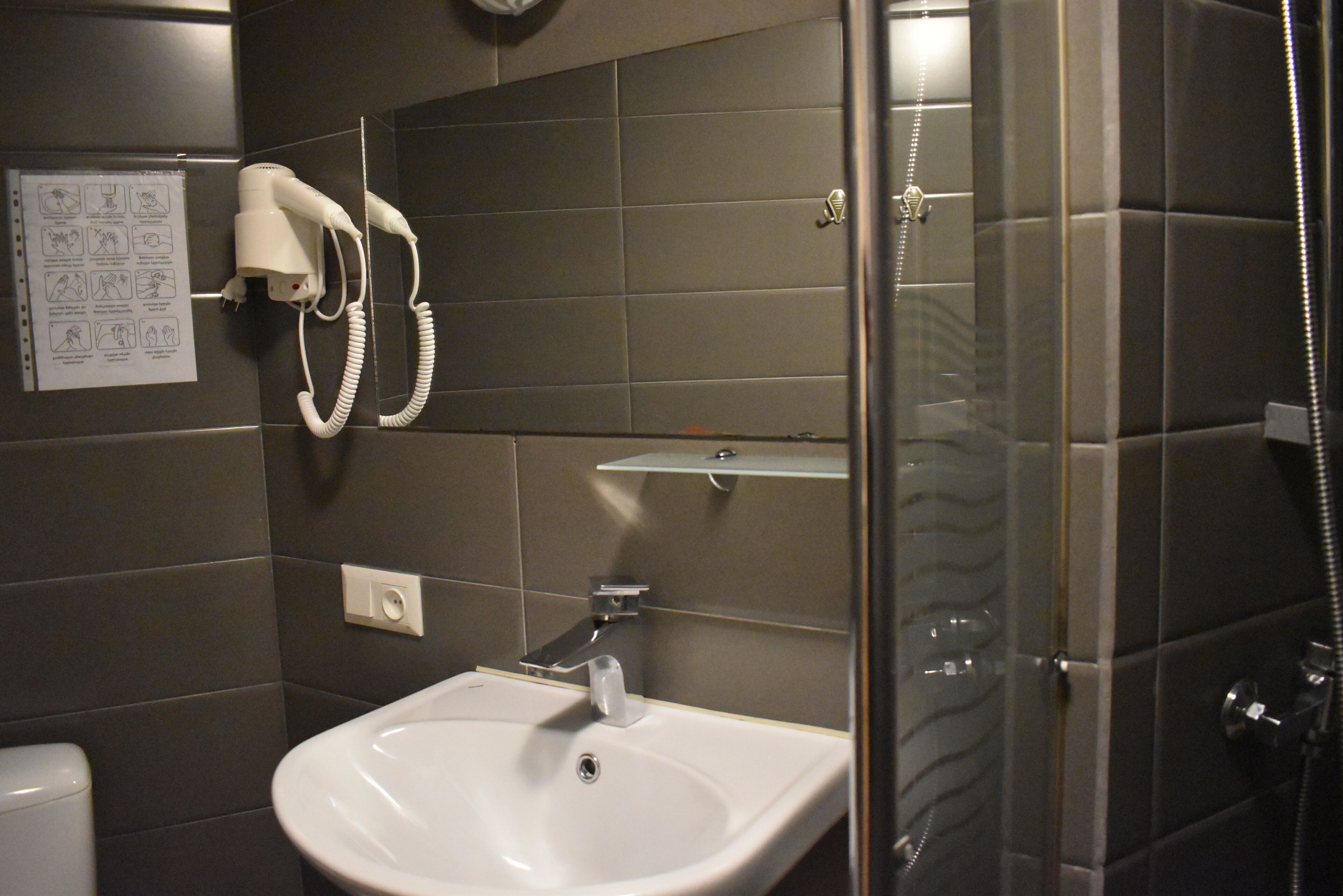 A bathroom with a white sink, a hairdryer mounted on the wall, and a glass shower enclosure.