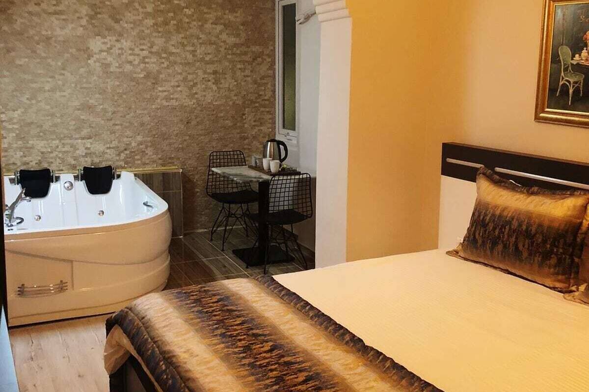 A hotel room with a bed, a sitting area with a table and chairs, a hot tub, and an air conditioning unit.